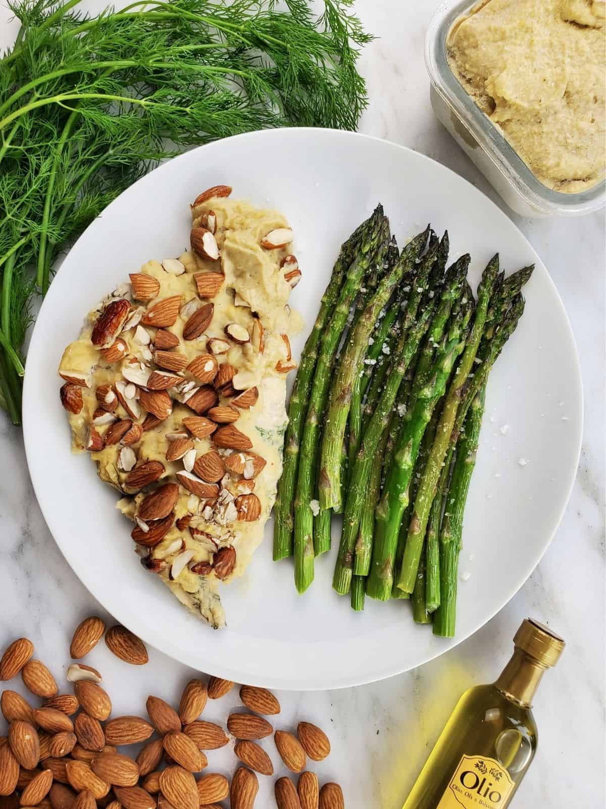 a plate of baked chicken covered in hummus, served with cooked asparagus.