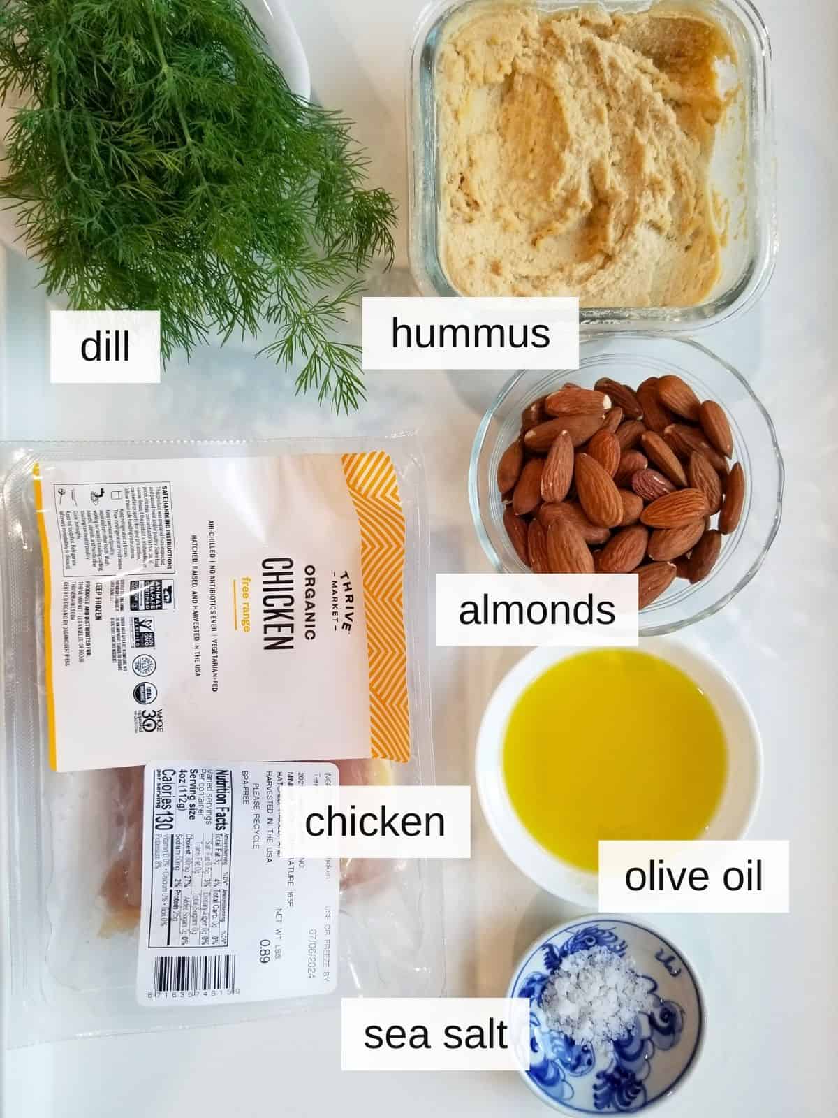 ingredients for baked hummus chicken, including hummus, almonds, fresh dill, chicken, olive oil, and sea salt.