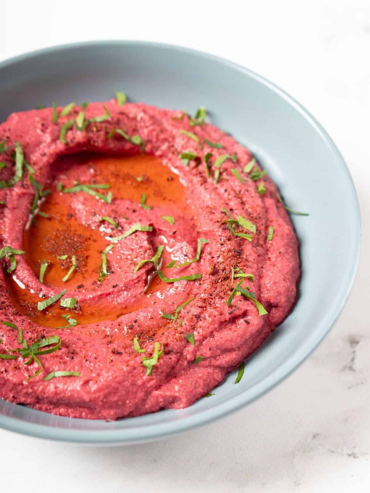 a bowl of pink beetroot humm.us garnished with fresh herbs.