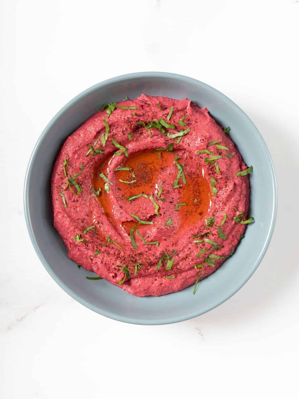 A bowl of pink beetroot hummus garnished with fresh herbs.