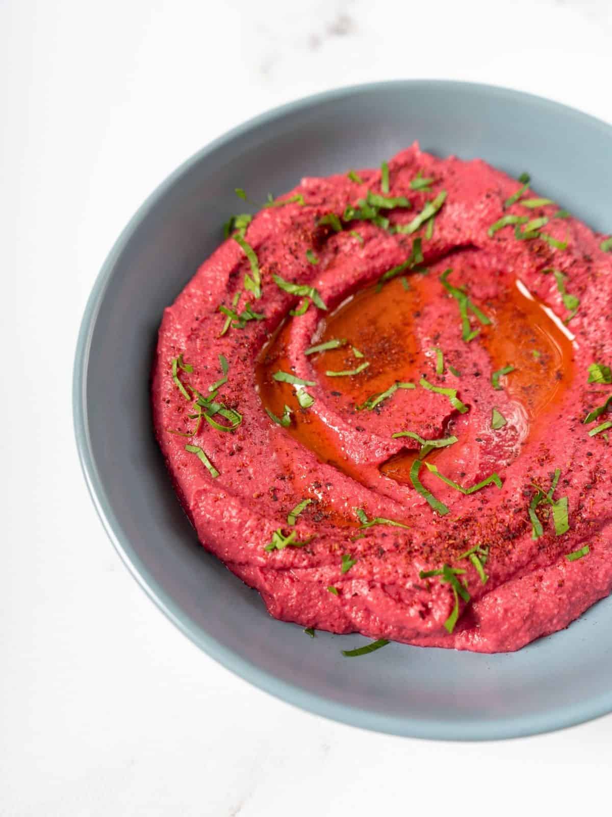 a bowl of pink beetroot humm.us garnished with fresh herbs.