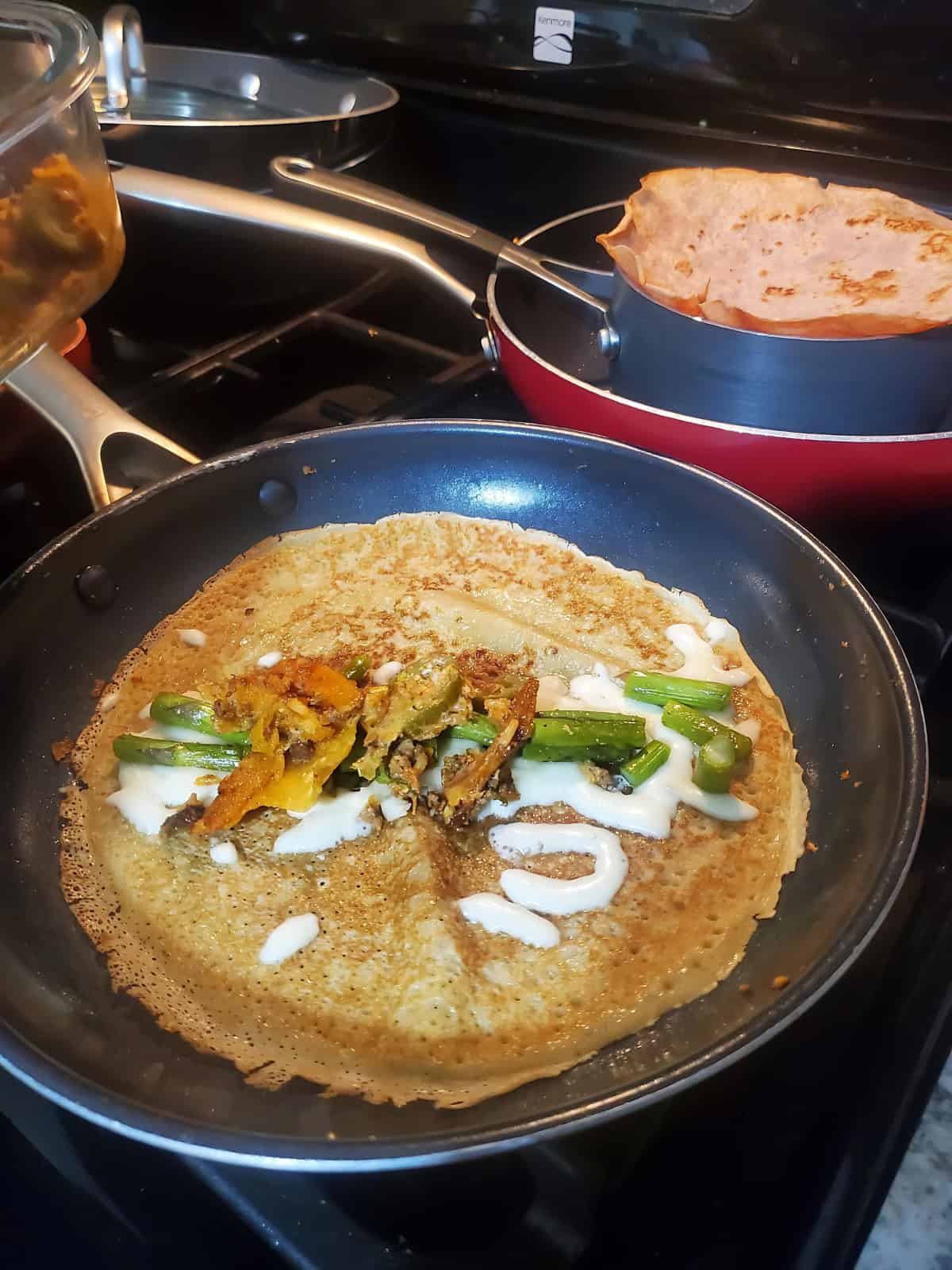 Crispy dosa on a pan topped with fried vegetables.