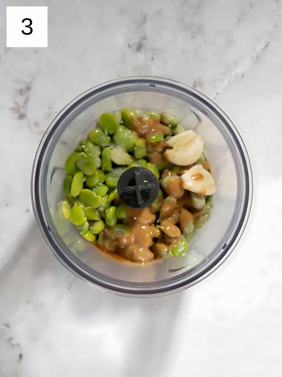 De-shelled and peeled fava beans with tahini and garlic cloves in a food processor.
