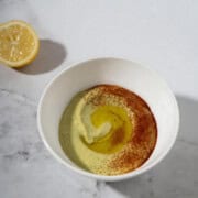 Fava bean hummus topped with paprika and olive oil next to a sliced lemon.