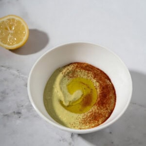 Fava bean hummus topped with paprika and olive oil next to a sliced lemon.