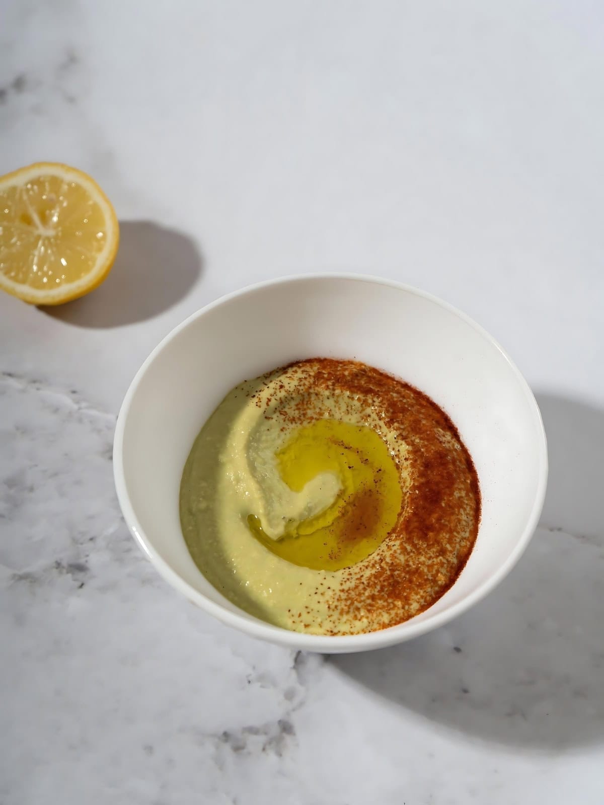 Fava bean hummus topped with paprika and olive oil next to a sliced lemon.