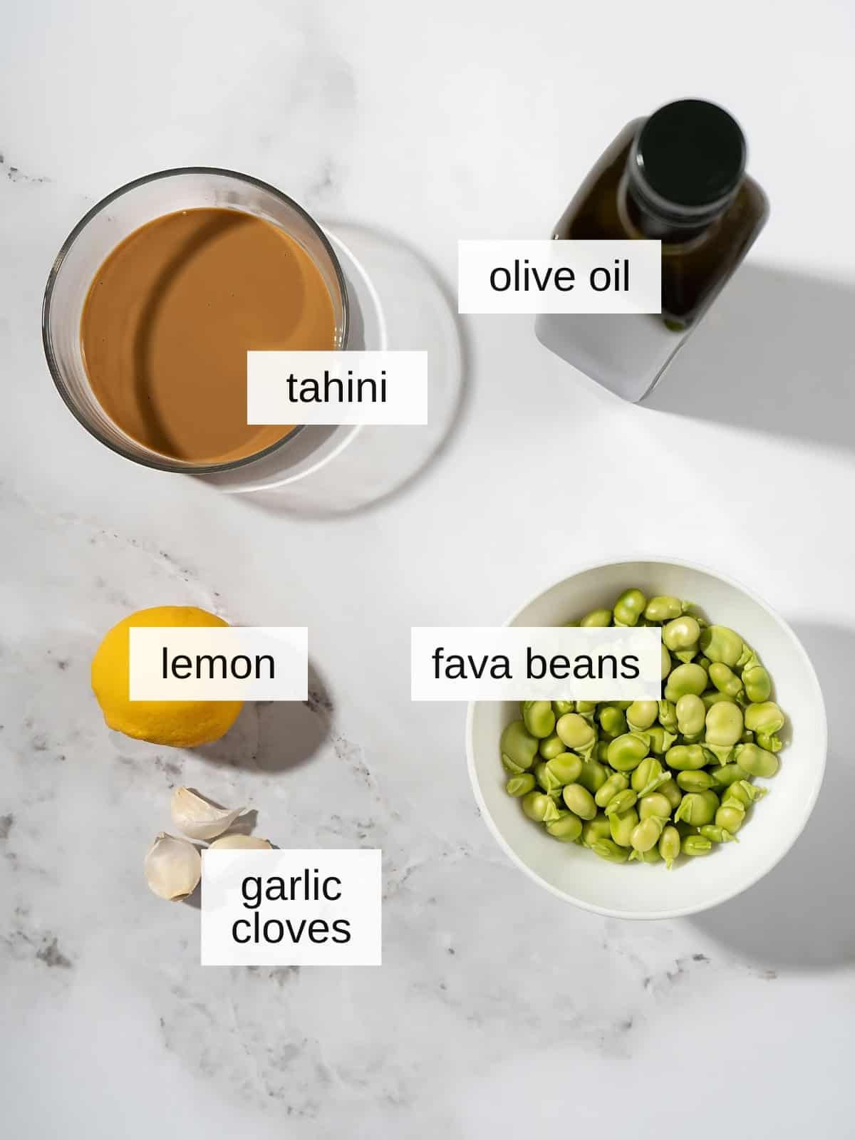 Fava bean hummus recipe ingredients with olive oil, tahini, fava beans, lemon, and garlic cloves.