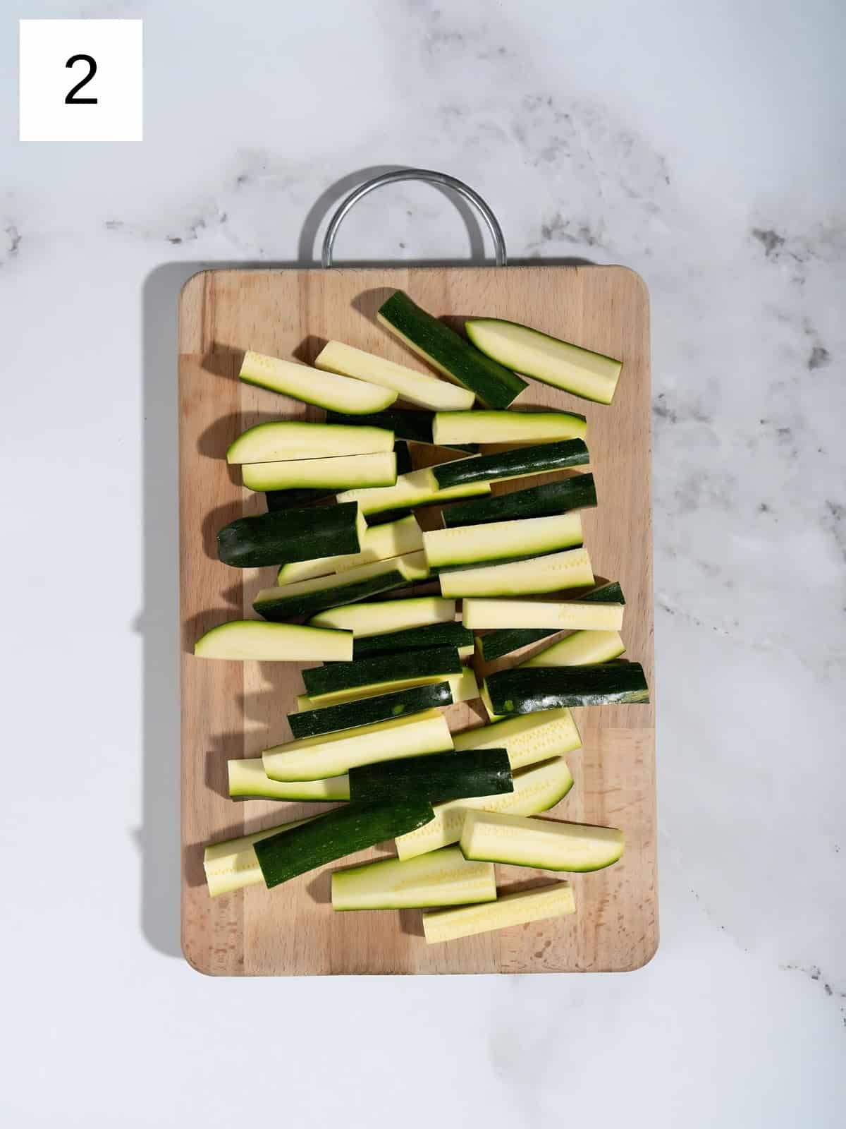 Zuccinis chopped into matchsticks on a chopping board.