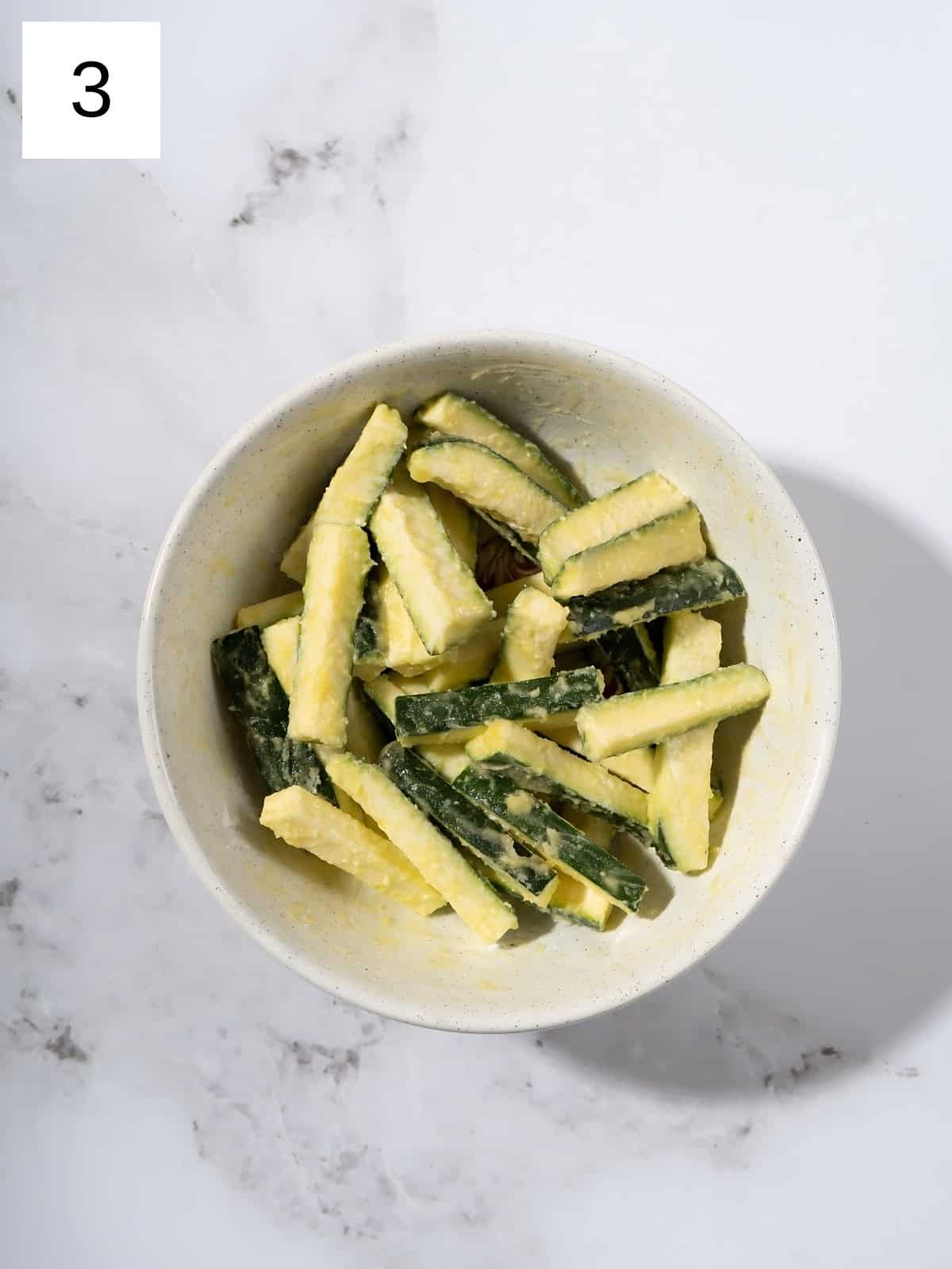 Chopped matchstick zucchinis covered with garlic powder in a bowl.