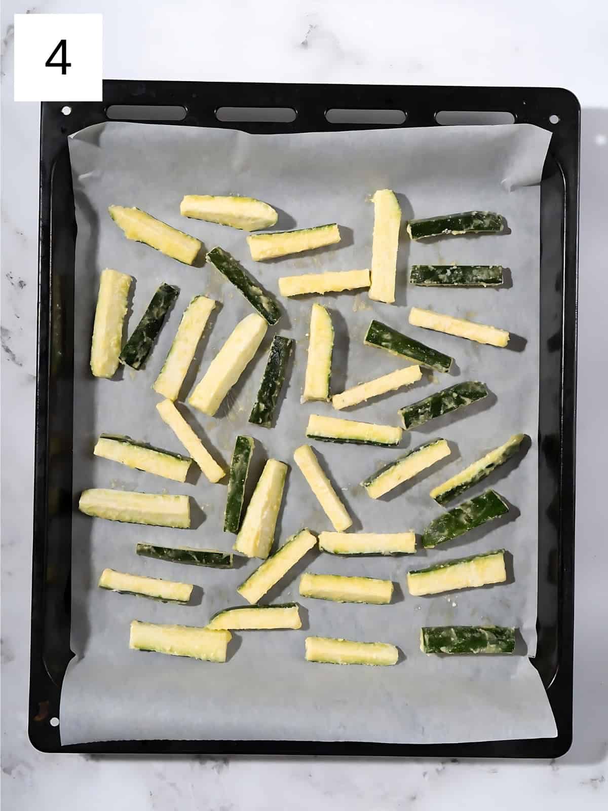 Zucchini fries covered with garlic powder on a baking tray.