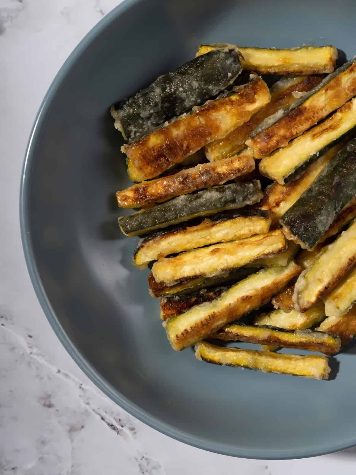 Crispy golden brown zucchini fries in a bowl.