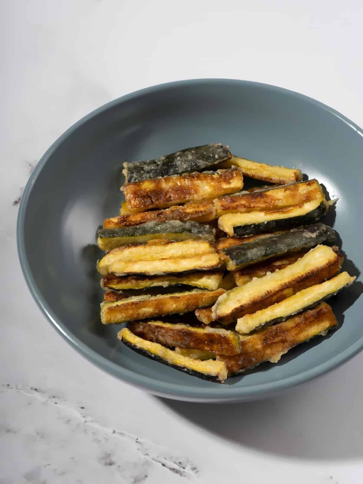 Crispy golden brown zucchini fries in a bowl.