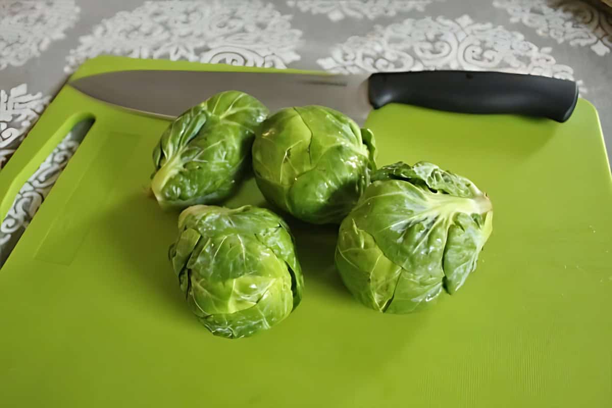 Brussel sprouts on a chopping board next to a knife. 