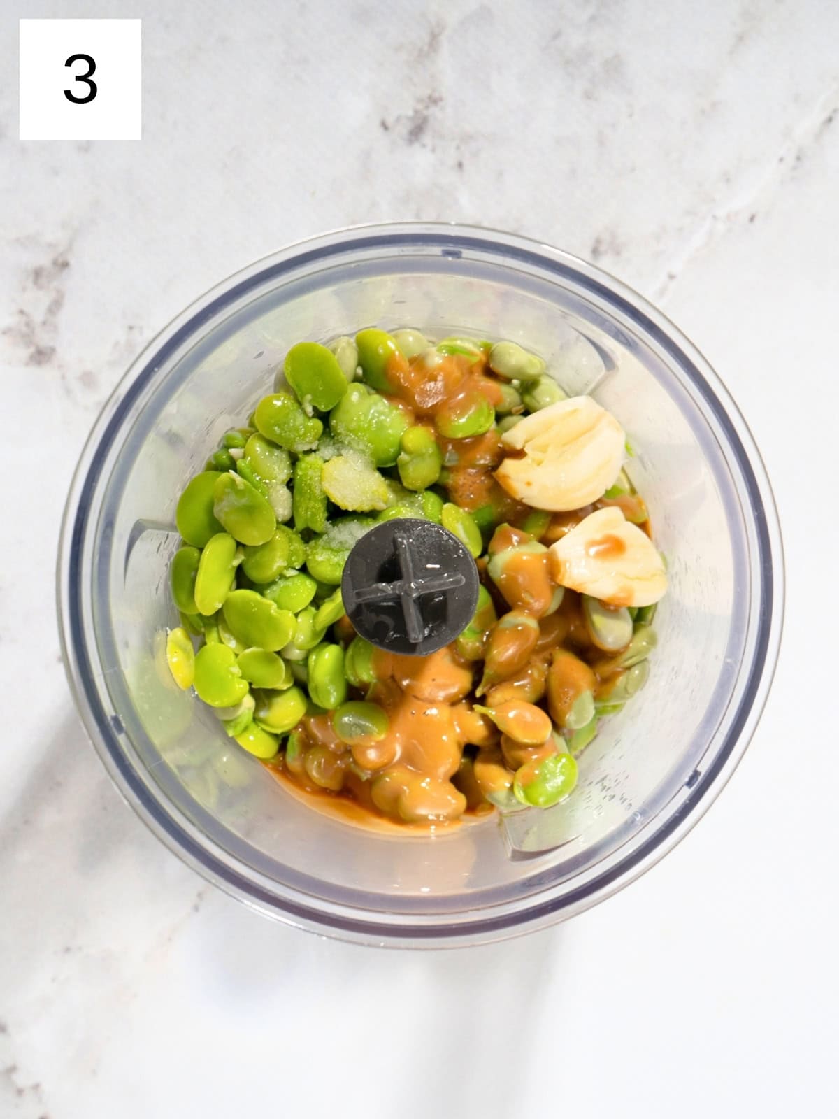 De-shelled and peeled fava beans with tahini and garlic cloves in a food processor.