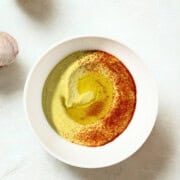 Fava bean hummus spiced with paprika with olive oil beside garlic and lemon.