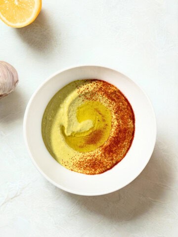 Fava bean hummus spiced with paprika with olive oil beside garlic and lemon.