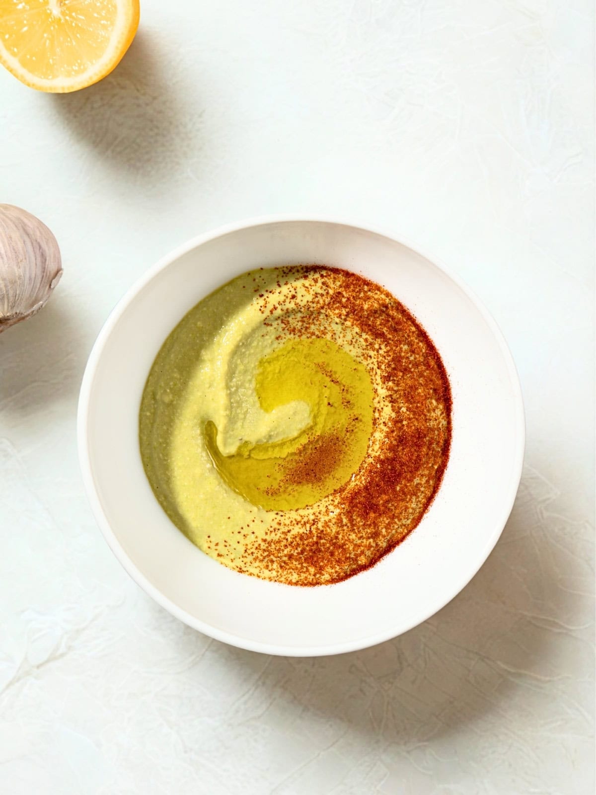 Fava bean hummus spiced with paprika with olive oil beside garlic and lemon.