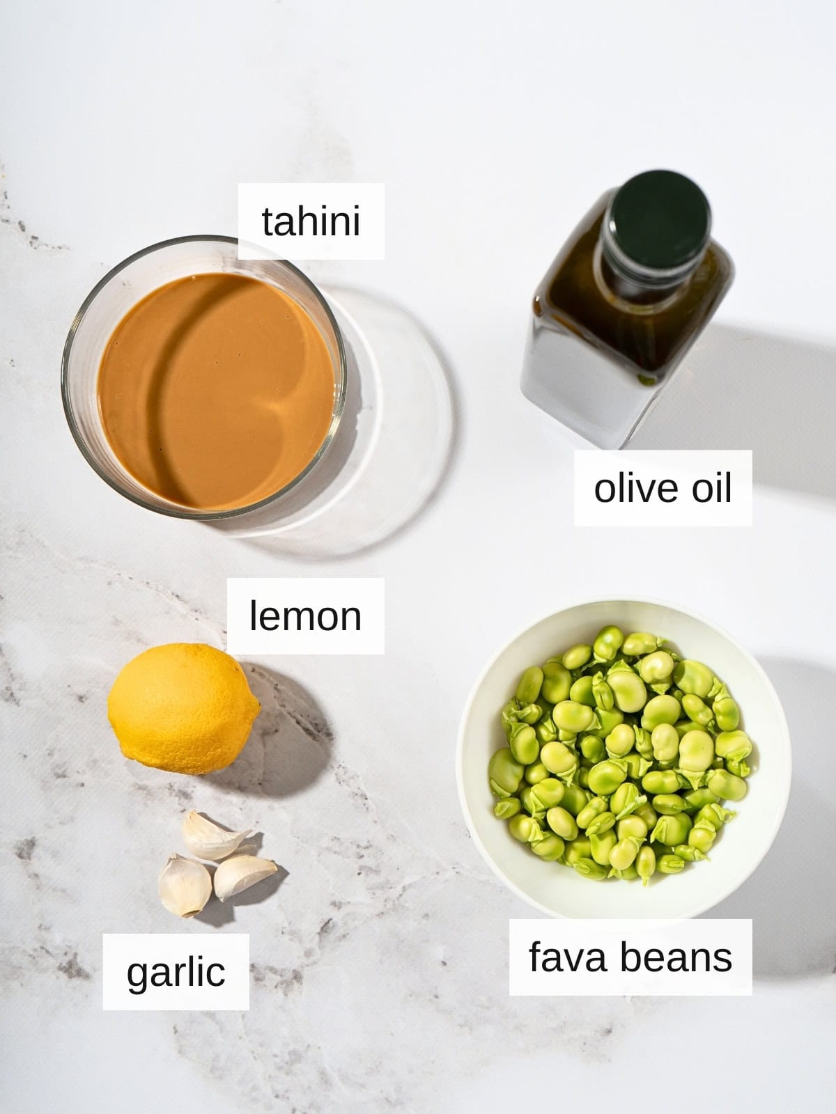 Fava bean hummus recipe ingredients with olive oil, tahini, fava beans, lemon, and garlic cloves.
