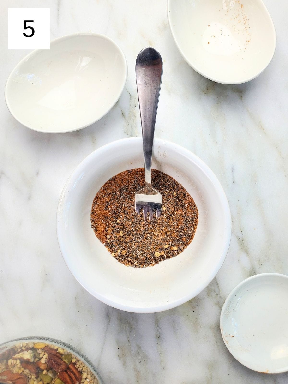 Chia seeds, vanilla powder, cinnamon, cardamom, and ginger powder being mixed with a fork.