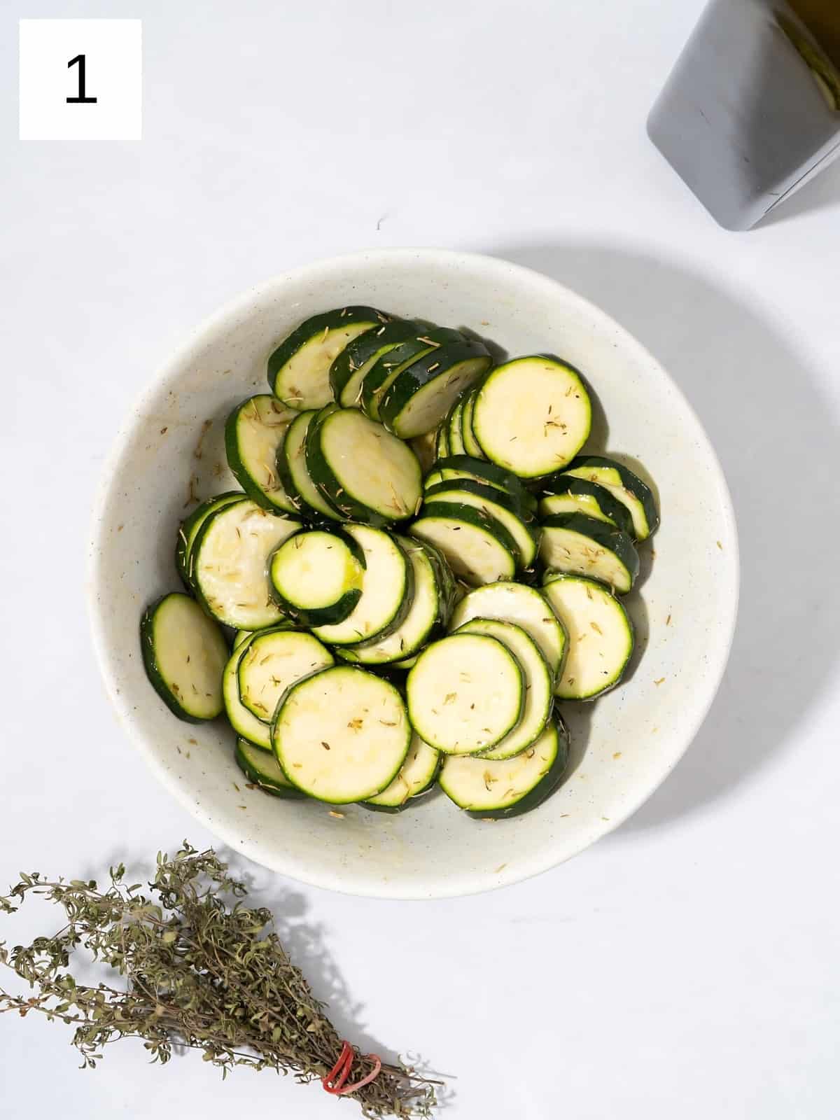 Disk cut zucchinis in a bowl coated with olive oil, rosemary, thyme and salt.