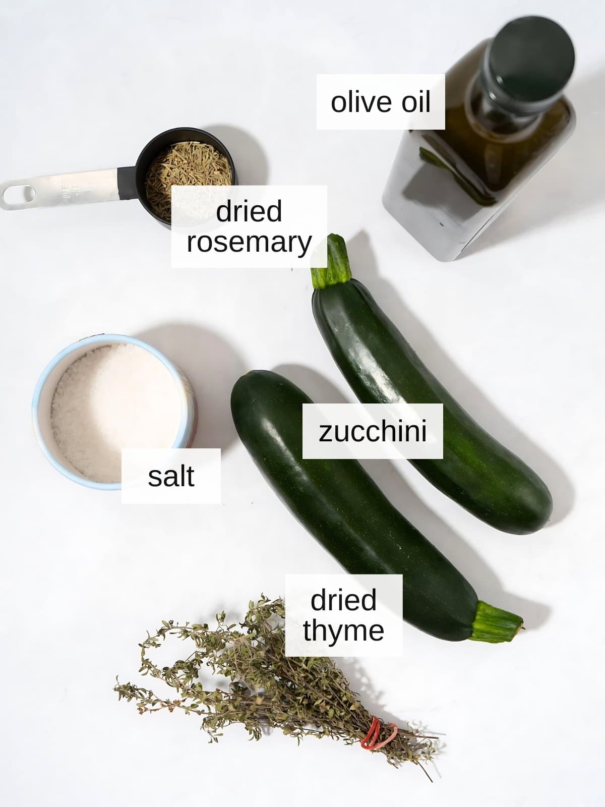 Herb roasted zucchini disks ingredients including olive oil, dried rosemary, dried thyme, salt, and zucchini.