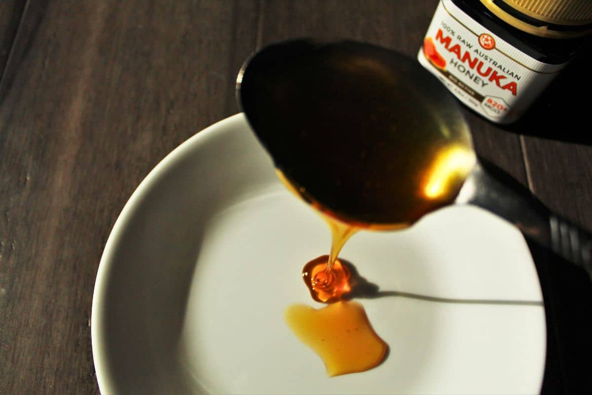 a spoonful of manuka honey being drizzled onto a white plate.