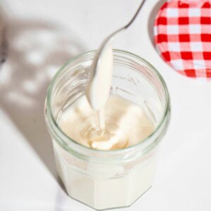 A spoon drizzling on top of a jar of creamed whipped honey.