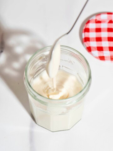 A spoon drizzling on top of a jar of creamed whipped honey.