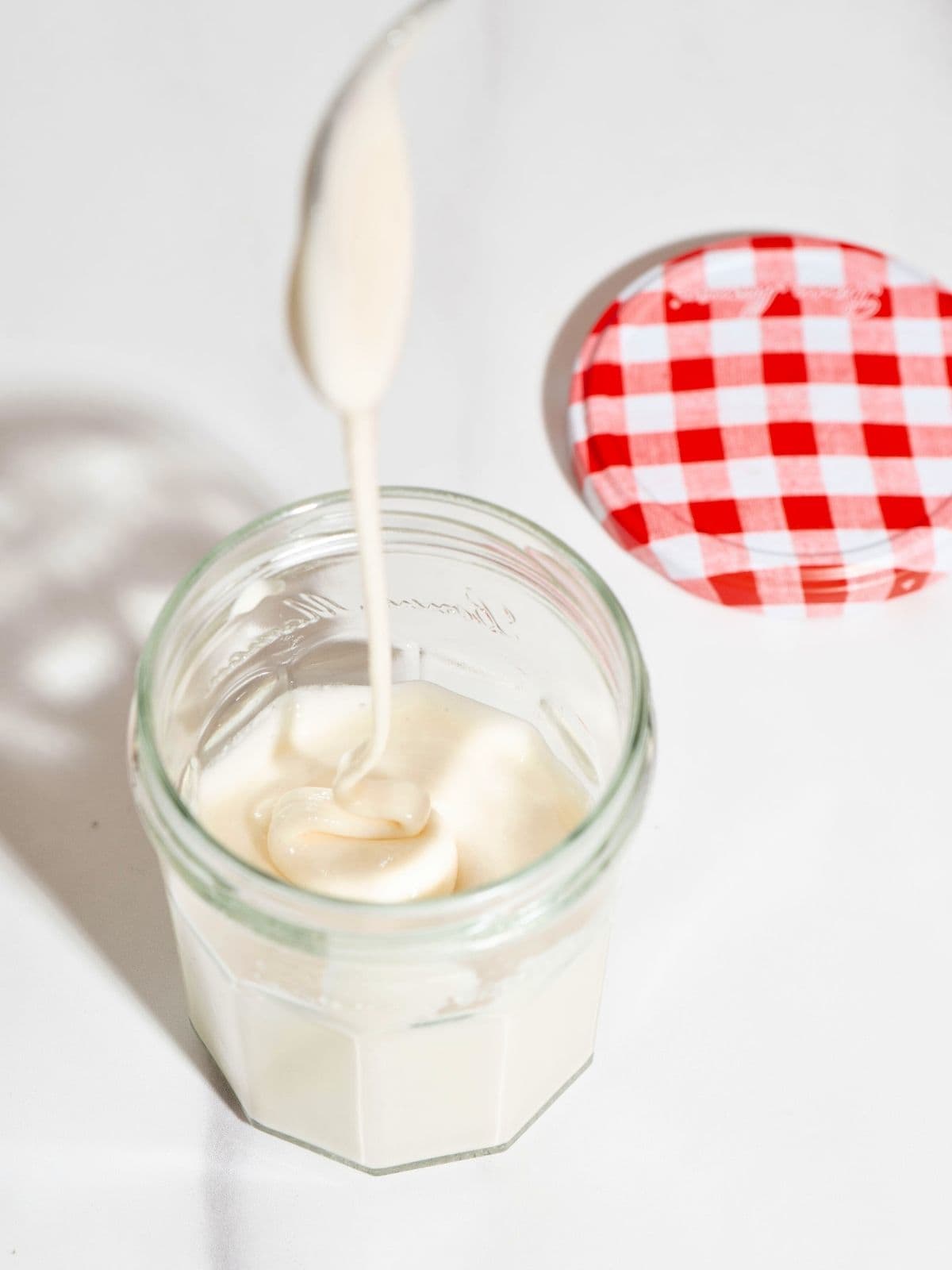 A spoon drizzling on top of a jar of creamed whipped honey.