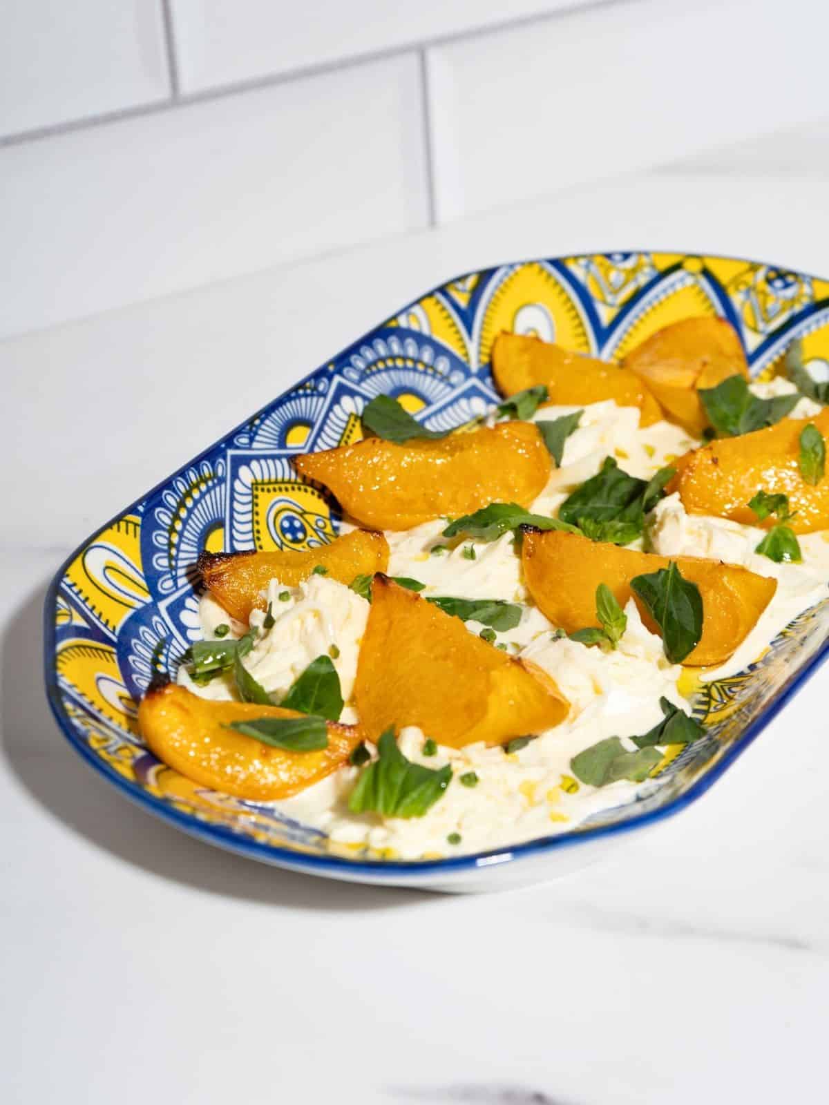 A platter of peaches with burrata topped with fresh herbs.