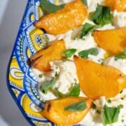 A platter of peaches with burrata topped with fresh herbs.