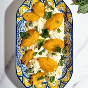 A platter of peaches with burrata topped with fresh herbs.