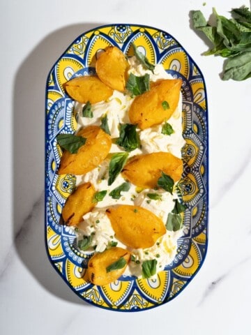 A platter of peaches with burrata topped with fresh herbs.