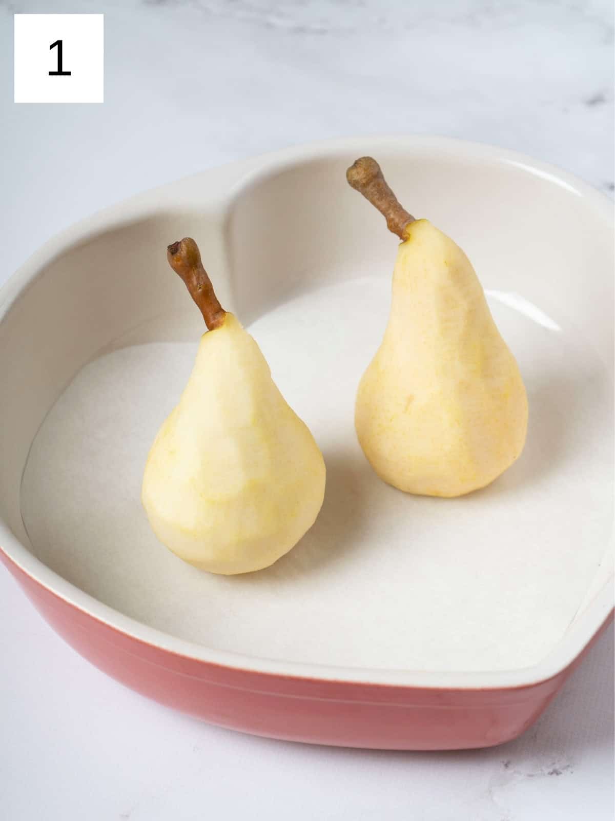 Two peeled pears placed upright in a baking dish, ready for baking, showcasing their smooth texture and inviting shape.

