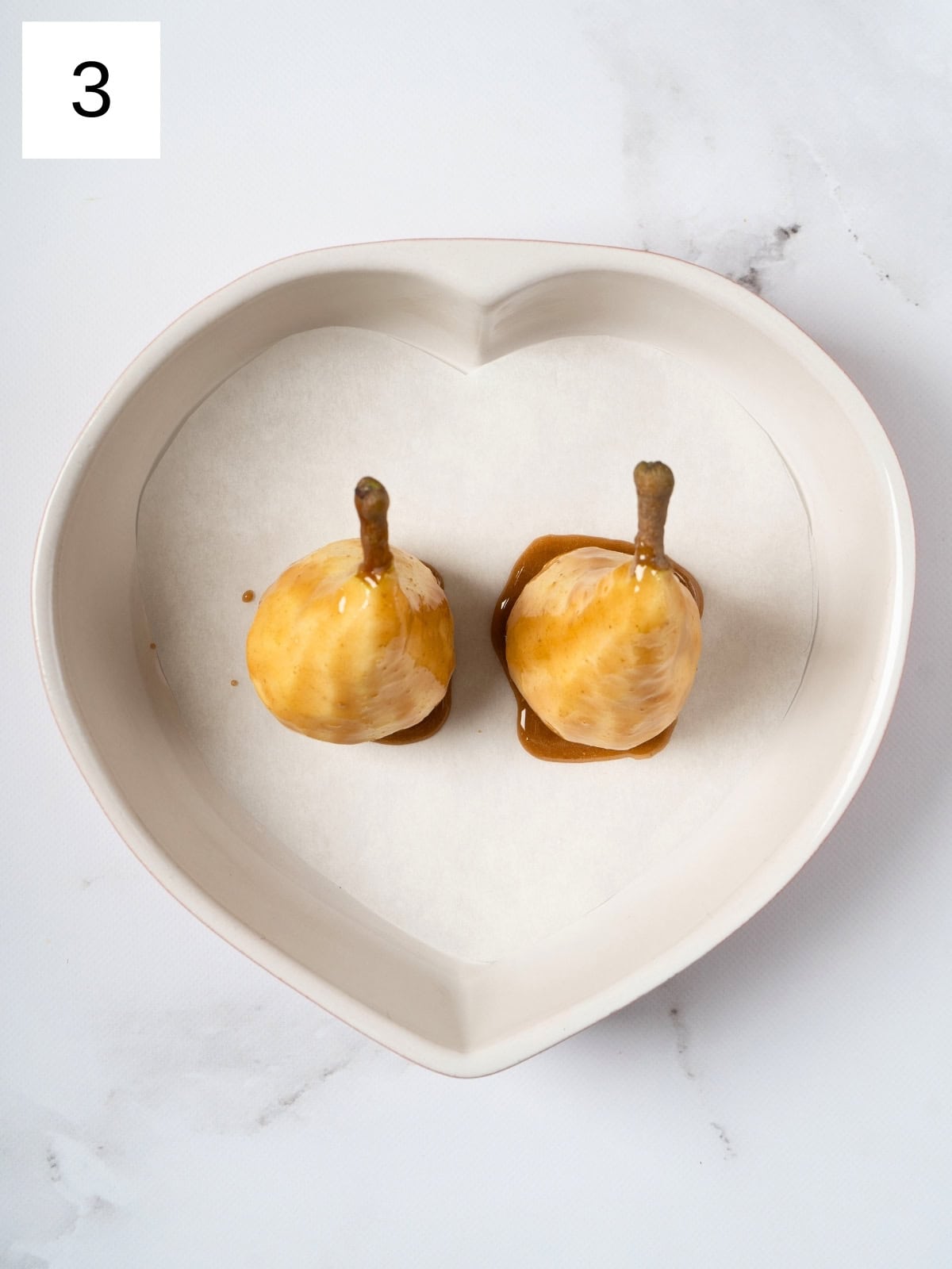 Two peeled pears drizzled with a golden honey mixture, glistening with spices, placed in a baking dish and ready to be baked to perfection.

