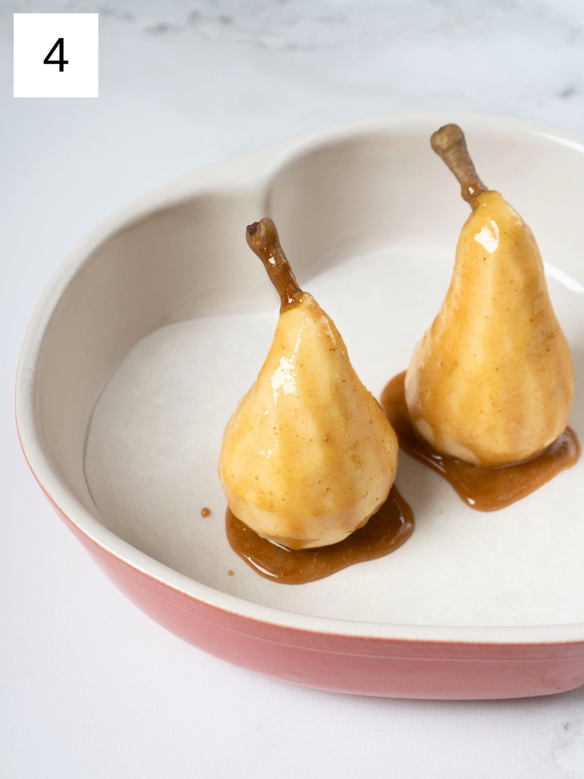 Two peeled pears drizzled with a golden honey mixture, glistening with spices, placed in a baking dish and ready to be baked to perfection.

