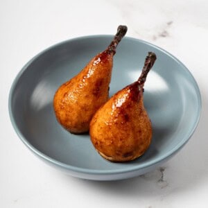 Whole baked pears, golden and tender, seasoned with a fragrant mixture of honey, cardamom, ginger, and lemon juice, beautifully arranged on a serving plate.