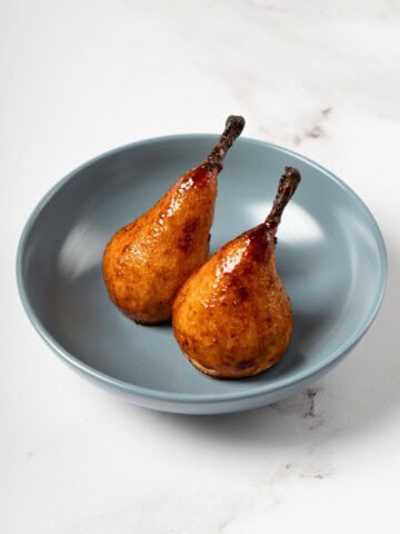 Whole baked pears, golden and tender, seasoned with a fragrant mixture of honey, cardamom, ginger, and lemon juice, beautifully arranged on a serving plate.