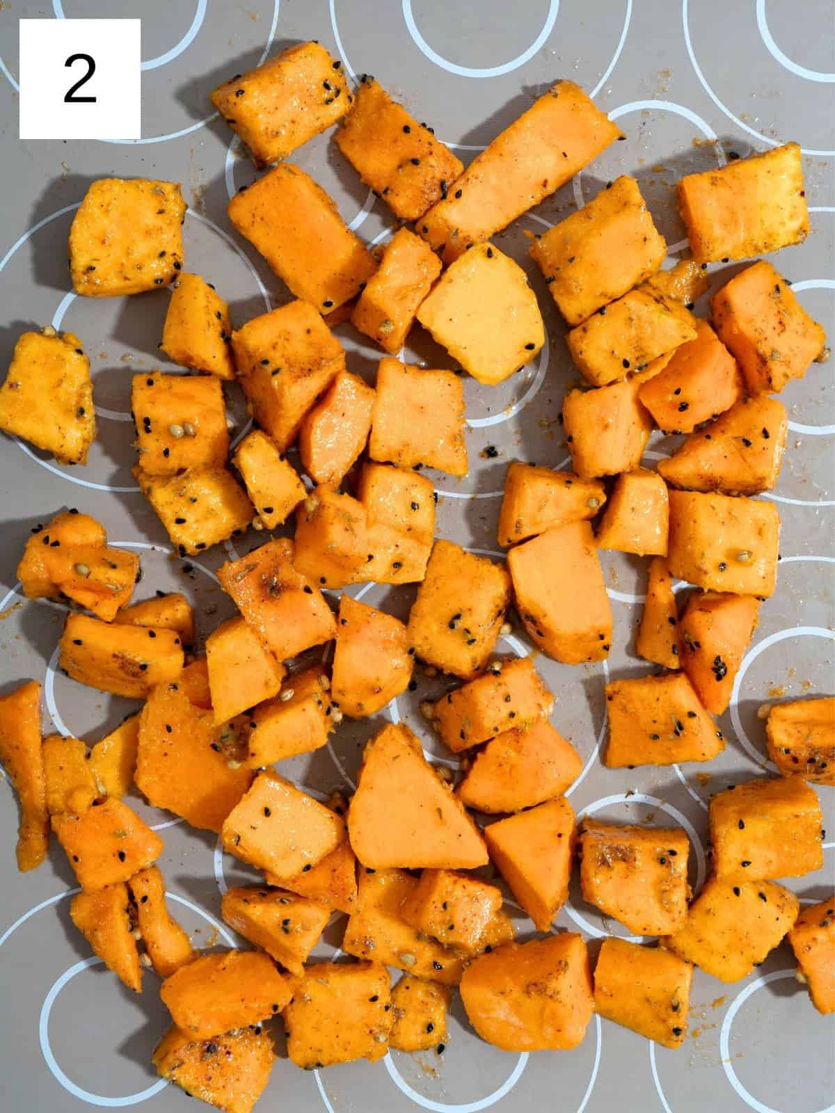 Seasoned butternut squash pieces layered on a baking tray.