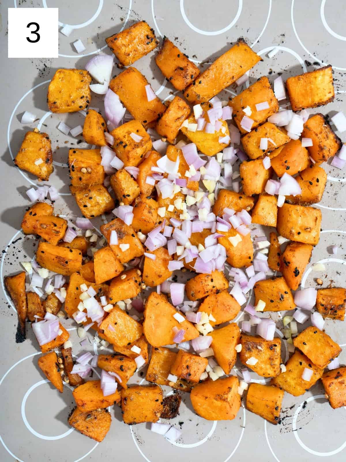 Chopped shallot and garlic mixed with seasoned butternut squash on a baking tray.