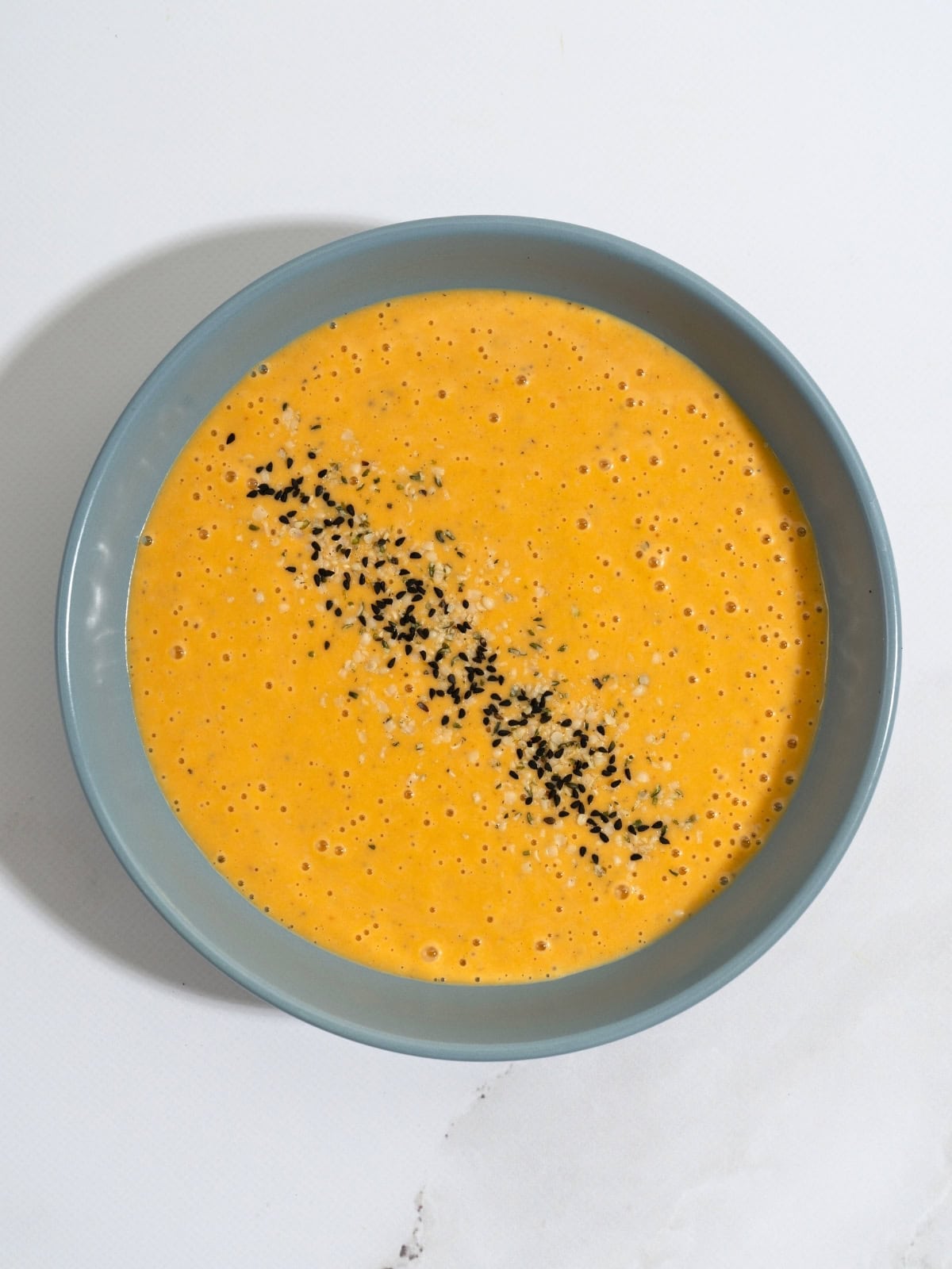 A bowl of butternut squash tahini soup, topped with seeds.