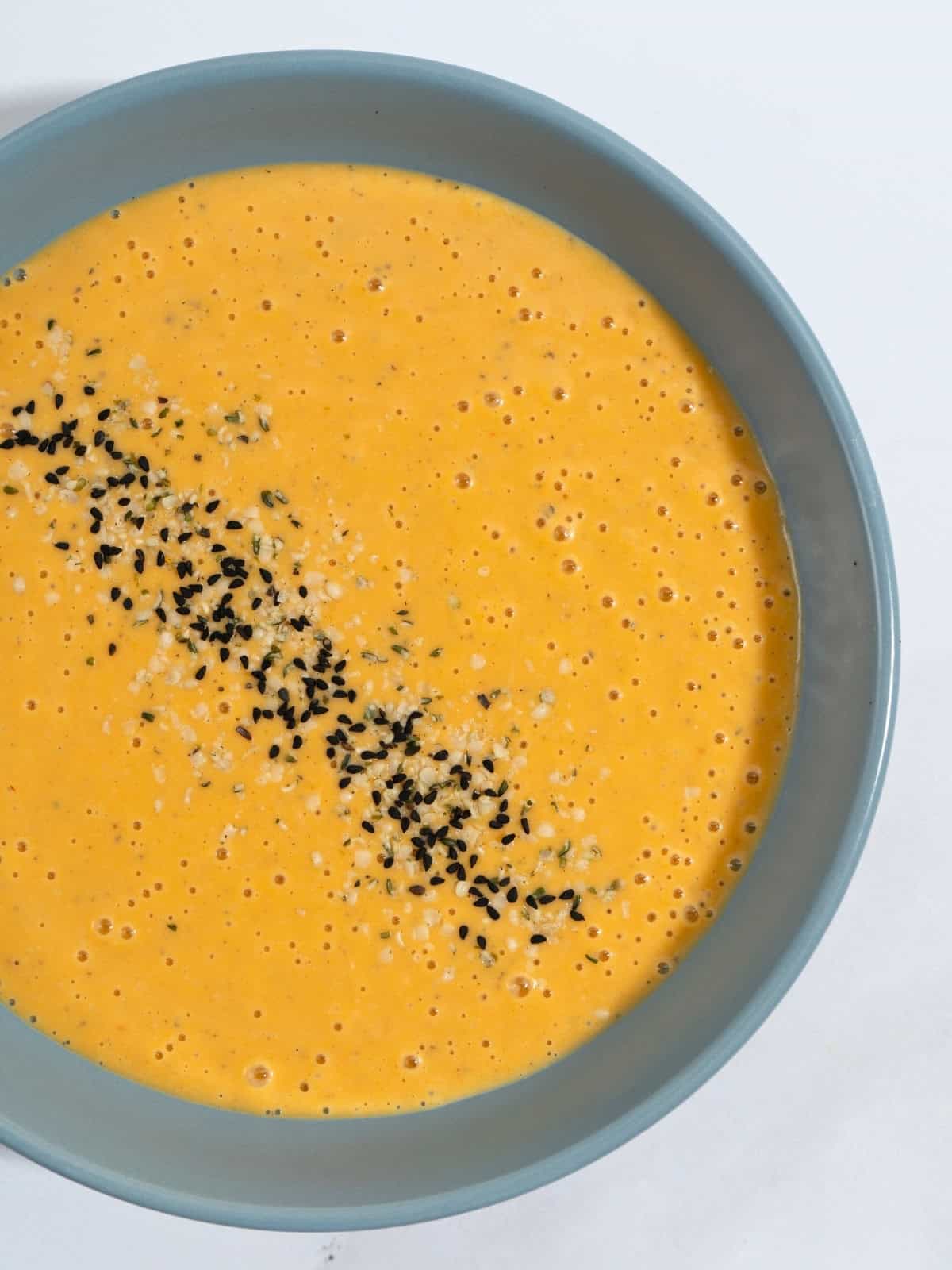 A bowl of butternut squash tahini soup, topped with seeds.