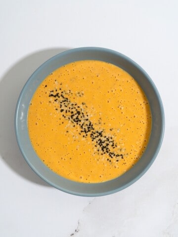 A bowl of butternut squash tahini soup, topped with seeds.