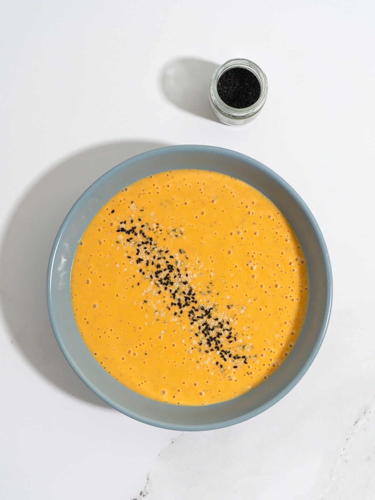 A bowl of butternut squash tahini soup, topped with seeds.