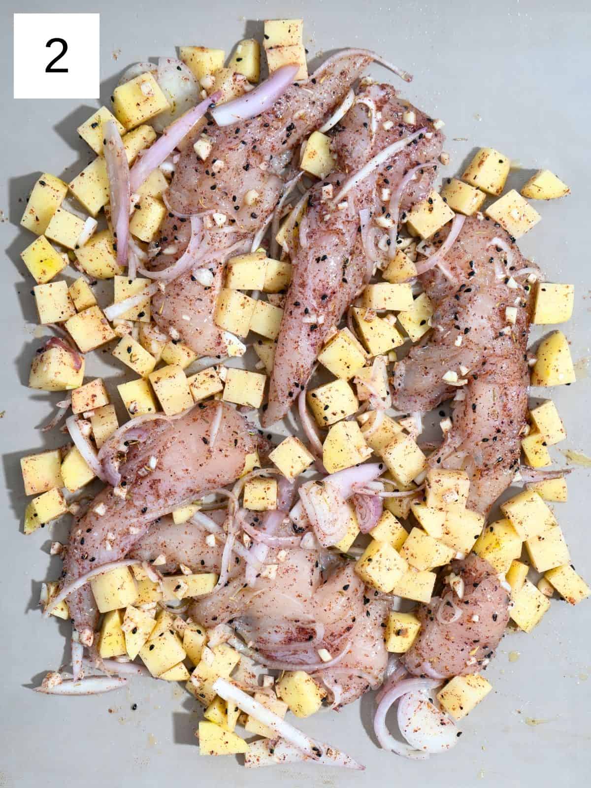 Seasoned chicken strips with potato slices, layered on a baking tray.