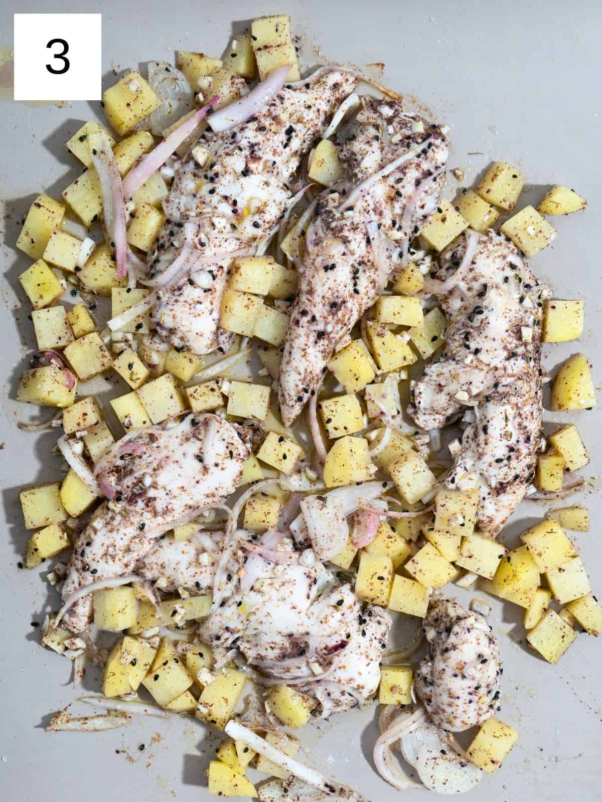 Baked seasoned chicken strips with potato slices, layered on a baking tray.