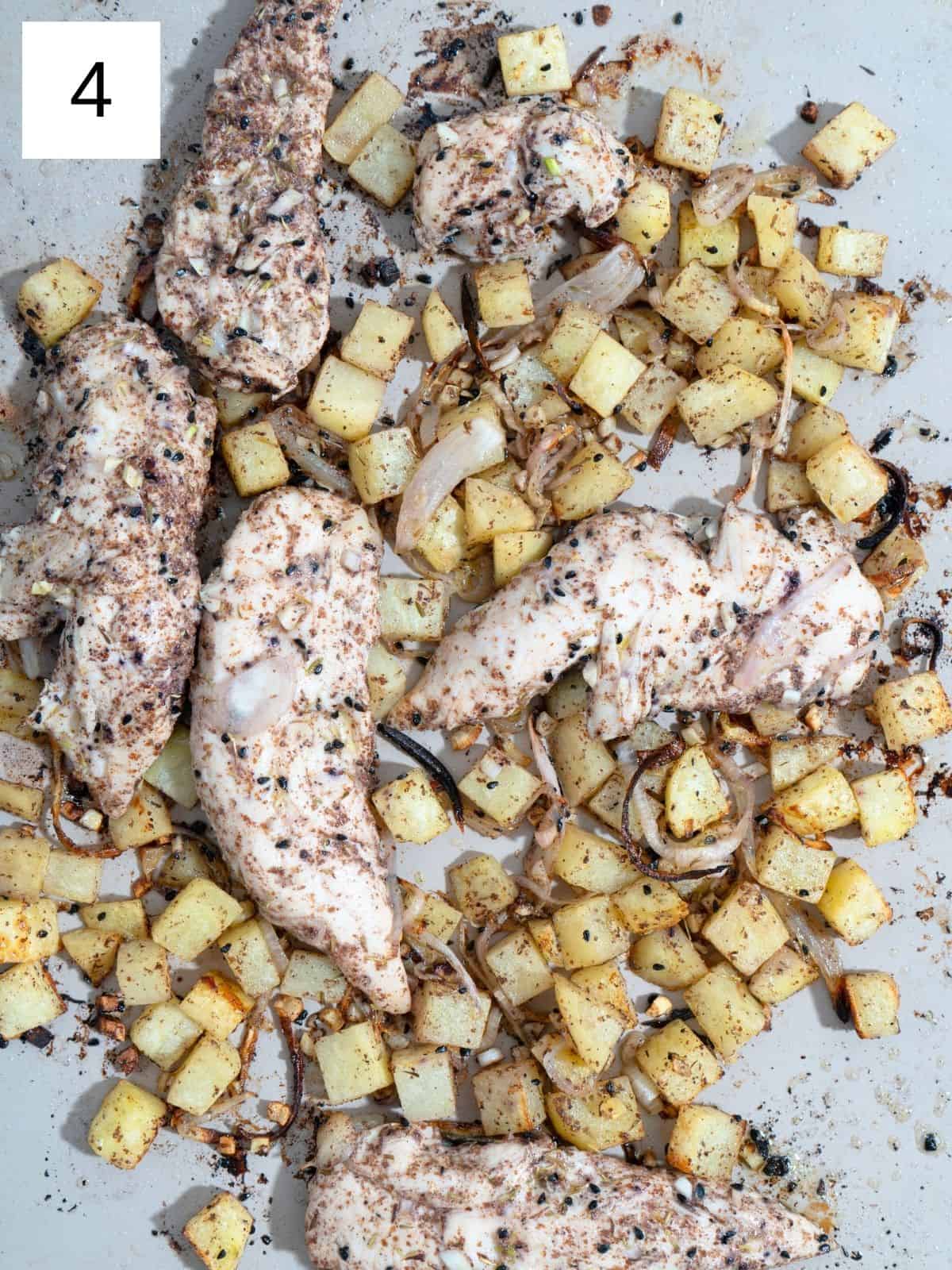 Baked seasoned chicken strips with potato slices, layered on a baking tray.