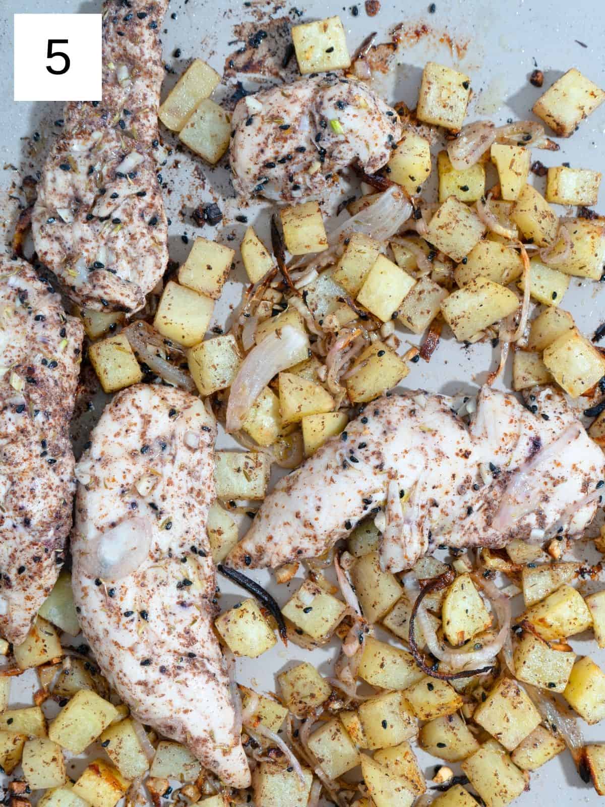 Baked seasoned chicken strips with potato slices, layered on a baking tray.