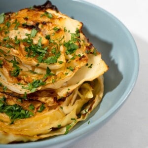 A plate of roasted cabbage steaks, with perfectly crispy edges, garnished with a sprinkle of herbs.