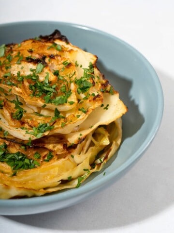 A plate of roasted cabbage steaks, with perfectly crispy edges, garnished with a sprinkle of herbs.